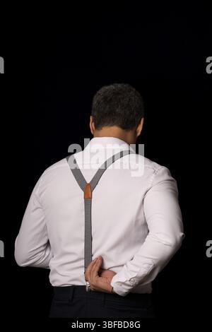 A man in a white shirt and black pants is wearing a black and white striped tie. He is bending over and adjusting his tie Stock Photo