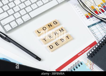 Long term debt concept with letters on cubes. Still life of office workplace with supplies. Flat lay white surface with computer keyboard and financia Stock Photo