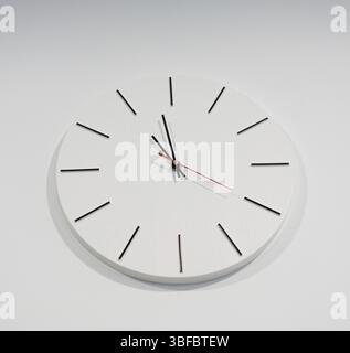 White round clock hangs on a light wall Stock Photo