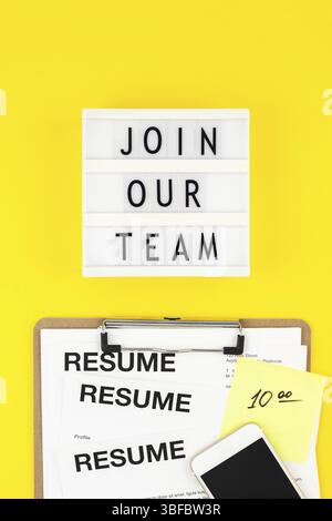 Creative top view flat lay of desk with join our team text on lightbox copy space on bold yellow background in minimal style. Concept of new job, hiri Stock Photo