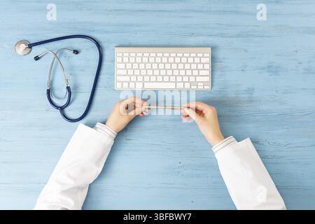 Top view of doctor hands holding pen. Physician in medical uniform working at blue wooden desk. Examination and diagnosis in hospital. Practitioner wo Stock Photo