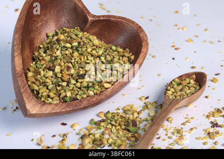 Crushed pistachio nuts in wooden bowl and heart-shaped spoon for cooking. Environmentally friendly product and health. Stock Photo