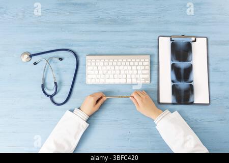 Top view of doctor hands holding pen. X-Ray radiography examination in hospital. Physician sitting at blue wooden desk. Examination and consultation i Stock Photo