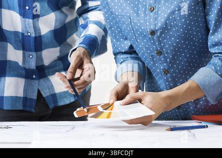 Interior designers discussing color samples for design project. Close up man hand with pencil pointing on color palette. Professional building, decora Stock Photo