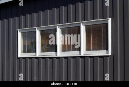 Four horizontal windows running across a dark corrugated wall of a building Stock Photo