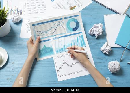 Corporate consultant analyze financial diagram. Close up woman hand with pen and coffee cup on blue wooden desk. Analyst in suit working at workplace Stock Photo