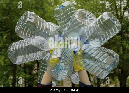 Garbage collection. Hands in yellow gloves holding big empty plastic bottles. Trees on a background Stock Photo