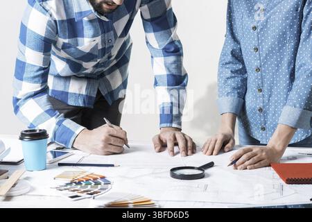 Man writing with pen on technical drawing. Creative team of designers together working with construction blueprint. Thorough study and approval of des Stock Photo