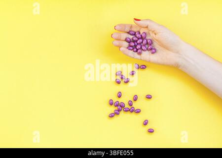 Woman hand holding purple pills handful isolated on bold yellow background with copy space. Template for feminine beauty blog social media. Female hea Stock Photo