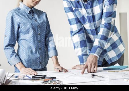 Man and woman together working at design project. Creative teamwork at workspace with construction blueprint and color swatches. People standing near Stock Photo