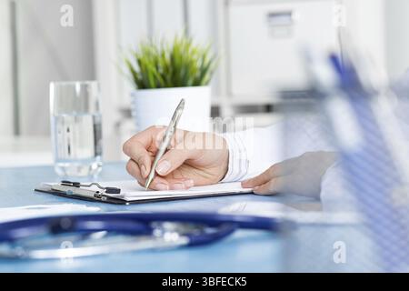 Close-up of female doctor filling medical form at clipboard. Therapist working at desk in office. Examination and diagnosis in modern clinic. Doctor w Stock Photo