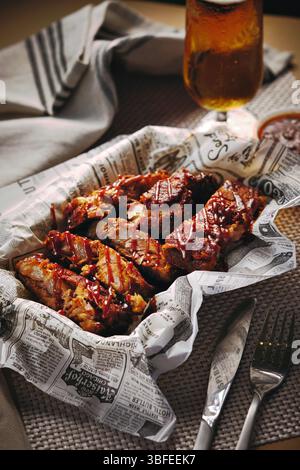 Close-up of glazed pork ribs served on rustic paper with sauce and beer Stock Photo