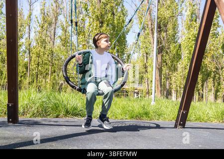 A boy is swinging on a round swing in a park. themes of childhood, outdoor activity, and recreation. Stock Photo