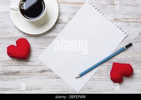 Coffee cup notepad pencil and two red hearts on wooden surface Stock Photo