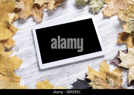 Tablet computer with blank screen lies on vintage wooden desk with bright foliage. Flat lay composition with autumn leaves on white wooden surface. In Stock Photo