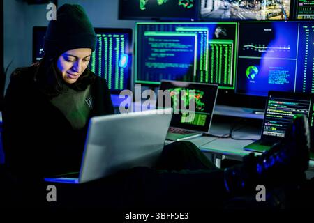 Female hacker breaking into corporate network using laptop and multiple screens Stock Photo