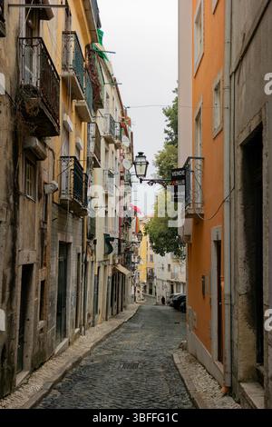 A narrow, paved street in the Alfama district of Lisbon, Portugal. The street is flanked by aged buildings constructed with stone and brick, exhibitin Stock Photo