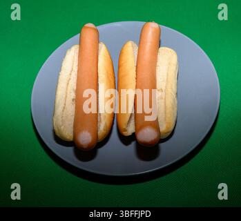 Two hot dogs placed in soft buns sit on a round gray plate. The vibrant green background adds a lively touch, perfect for a casual meal or gathering a Stock Photo