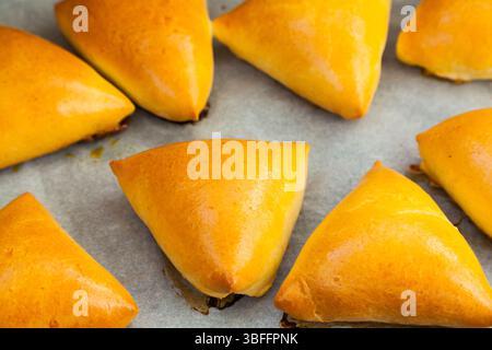 Homemade baked triangular buns lie on white parchment. Stock Photo