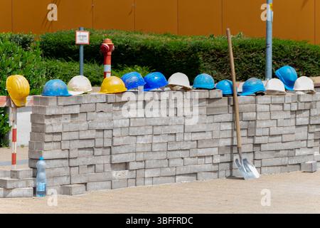 Construction site helmets: multi-coloured construction helmets neatly stacked on a wall of bricks symbolise safety and workflow on a construction site Stock Photo