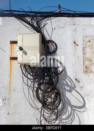 Tangled and messy wires hang from a junction box on a weathered wall, creating a chaotic and disorganized scene Stock Photo