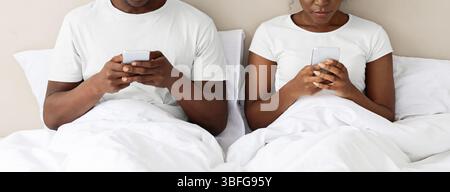 Unrecognizable black couple using smartphones in bed Stock Photo