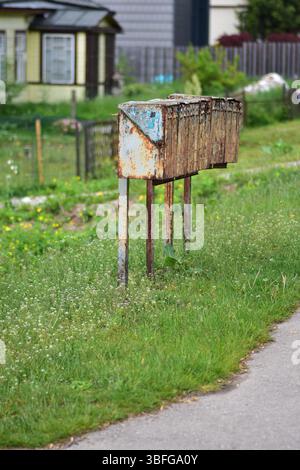 Row of old, rusty metal mailboxes on a rural roadside. Weathered and vintage appearance, surrounded by grass and greenery. Represents abandonment. Stock Photo