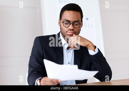 Pensive black manager sitting in office, reading papers Stock Photo