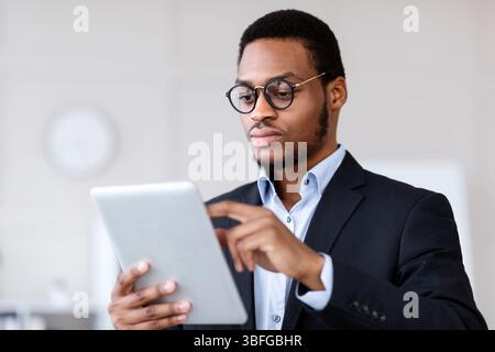 Serious black entrepreneur in glasses using digital tablet Stock Photo