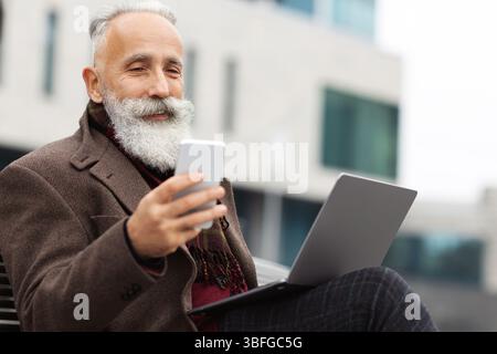 Senior businessman with laptop using smartphone outdoors Stock Photo