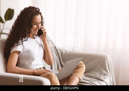 Woman freelancer talking on phone and using laptop Stock Photo