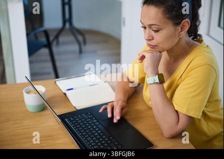 Confident self-employed woman working on a laptop while enjoying coffee. Home workspace conveys productivity and balance. Captures the essence of remo Stock Photo