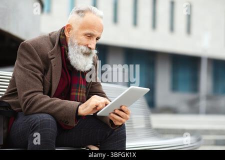 Stylish grey-haired man sitting on the bench, using digital tablet Stock Photo
