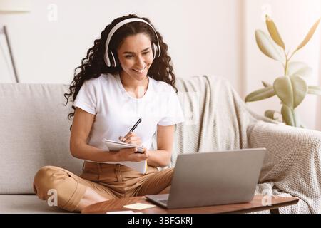 Cheerful lady attending webinar, using laptop and wireless headset Stock Photo