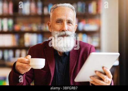 Wealthy senior businessman drinking coffee and using digital tablet Stock Photo