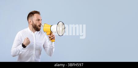Agitated young man screaming into megaphone on grey studio background Stock Photo