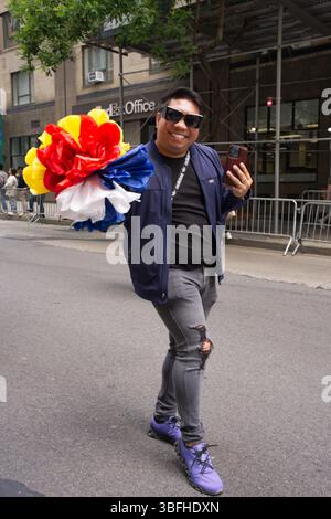 A man in a dark blue jacket, gray ripped jeans, and purple sneakers holds a large multi-colored pom-pom. He smiles at the camera while holding a smart Stock Photo