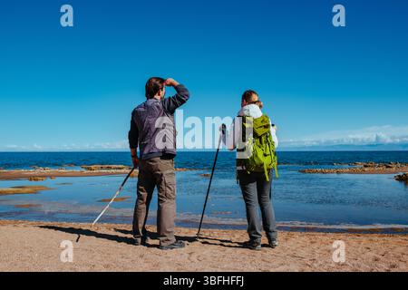 Man and woman tourists standing on lake shore and looking into the distance Stock Photo