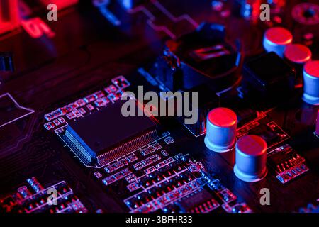 Close-up of a computer motherboard surface with chips, capacitors, and circuits illuminated in red and blue, creating a high-tech, intricate electroni Stock Photo