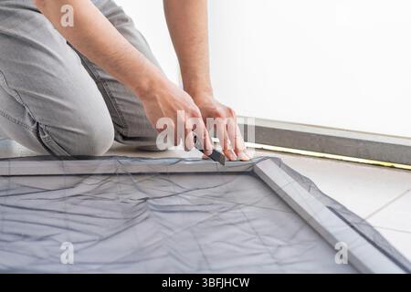 Man's hands installing a wire mosquito net on a door in his house to protect from insects.Mosquito net windows Stock Photo