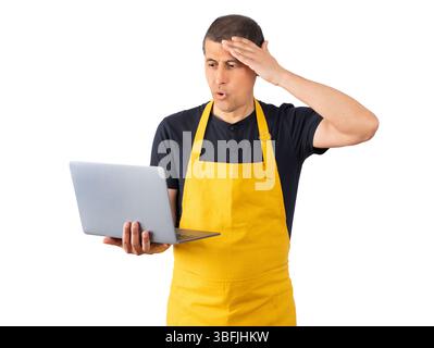 Man wearing employee yellow apron over isolated background using computer laptop stressed with hand on head, shocked with shame and surprise face, ang Stock Photo