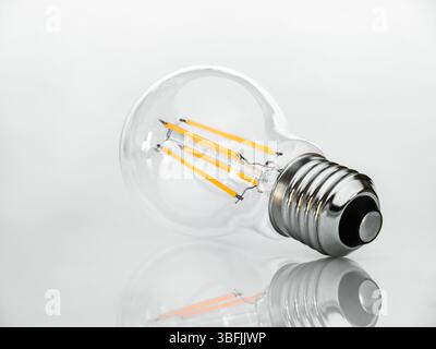 View from the base of the socket on a Filament type LED lamp isolated on a white background with reflection. Stock Photo