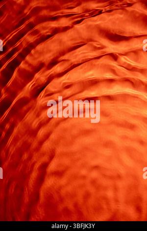 Vibrant orange water surface with gentle ripples creating a flowing texture Stock Photo