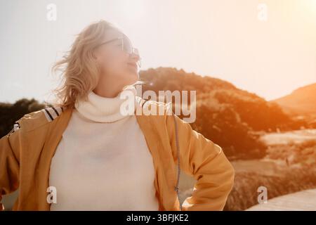 Woman, Sunshine, Landscape - Smiling Woman in Yellow Jacket Looking at the Sun Stock Photo