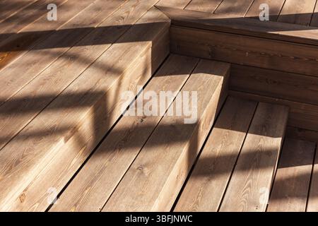 Wooden deck stairs are captured in soft natural daylight, showcasing their grain and texture. The shadows cast create an interesting interplay of shap Stock Photo