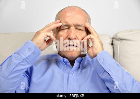 Senior man suffering headache and complaining sitting on a sofa in the living room of a house Stock Photo