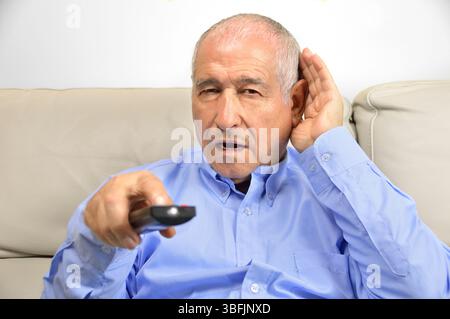 Senior man cupping his hand behind his ear to hear better to the television Stock Photo
