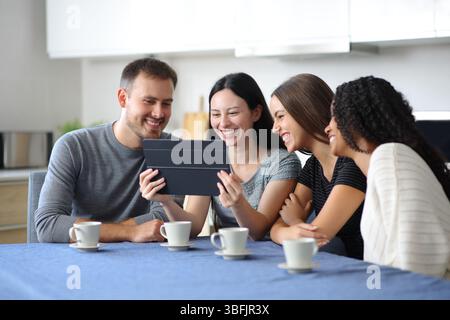 Happy interracial friends are checking tablet in a kitchen at home Stock Photo