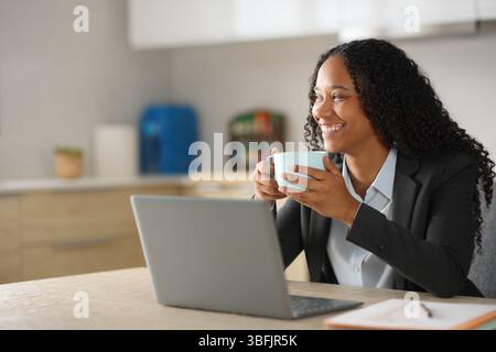Happy black executive taking a coffee break while working with laptop in the kitchen at home Stock Photo