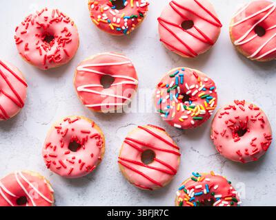 Top view of donuts with pink glaze and sprinkles on gray backdrop. Stock Photo